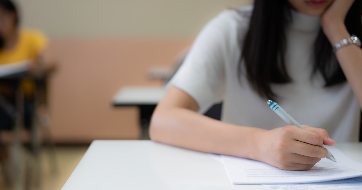 Ученица пишет ручкой на экзаменационном бланке за партой в классе во время симуляции экзамена