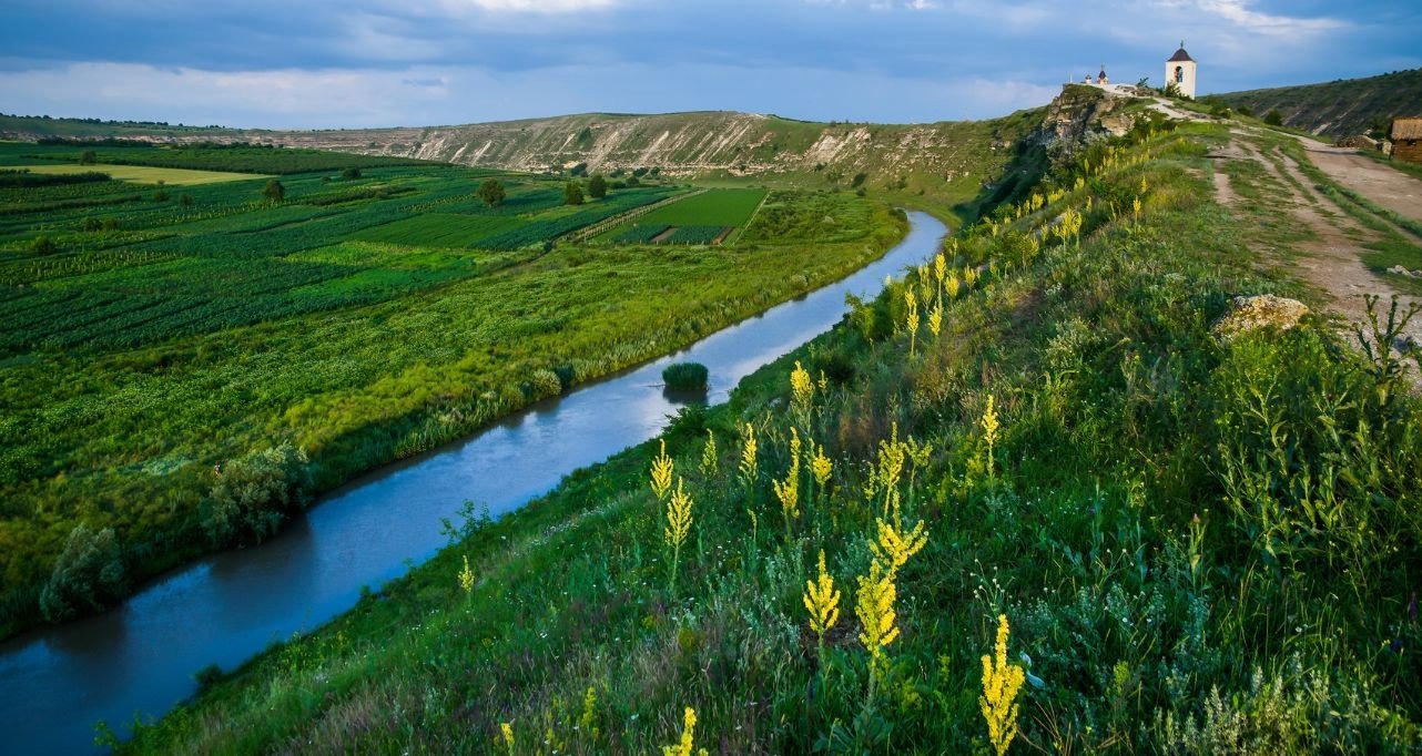 Живописный вид молдавской глубинки: извилистая река среди зелёных виноградников с церковью на холме