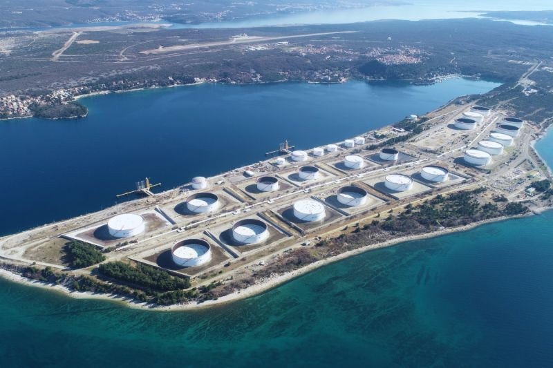 Aerial view of the Omisalj oil terminal on the Croatian coast with large white storage tanks on a peninsula surrounded by turquoise sea. Фото: CEE Energy News