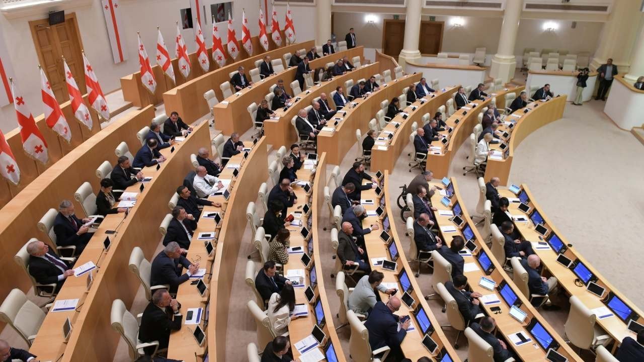 Заседание парламента Грузии — депутаты за рабочими столами в зале пленарных заседаний на фоне государственных флагов