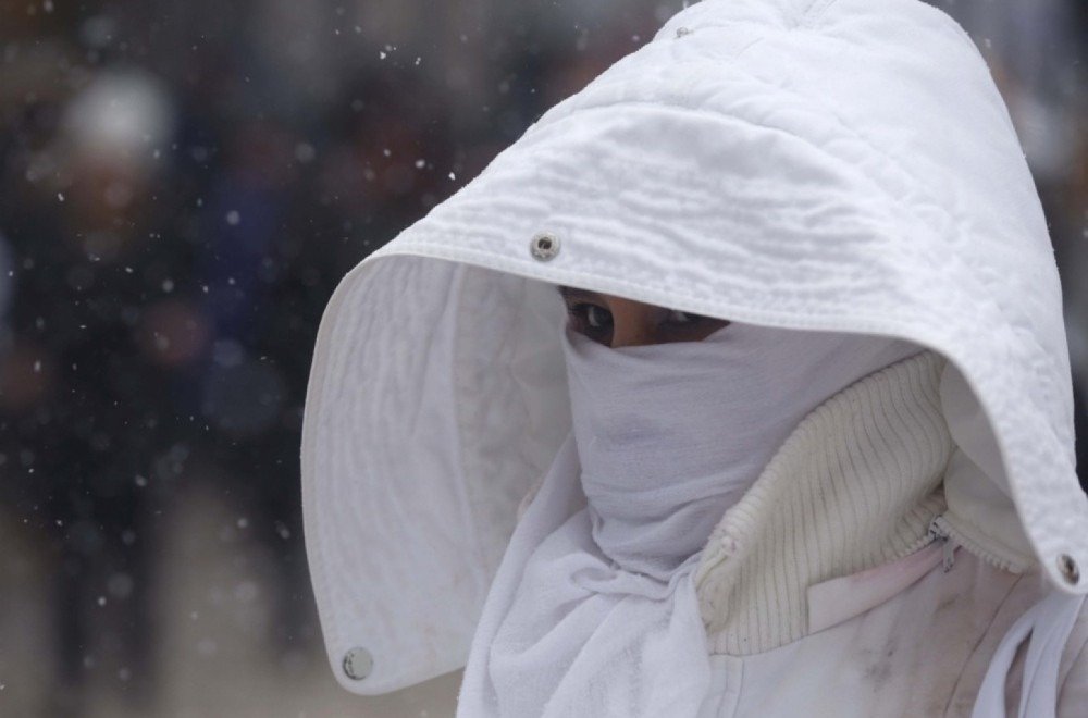 Человек в белом капюшоне укрывается от снегопада