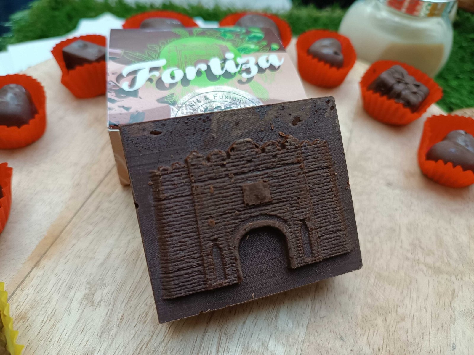 Безглютеновый шоколад в форме Нишской крепости с брендом «Fortiza» в окружении шоколадных конфет и фирменной упаковки