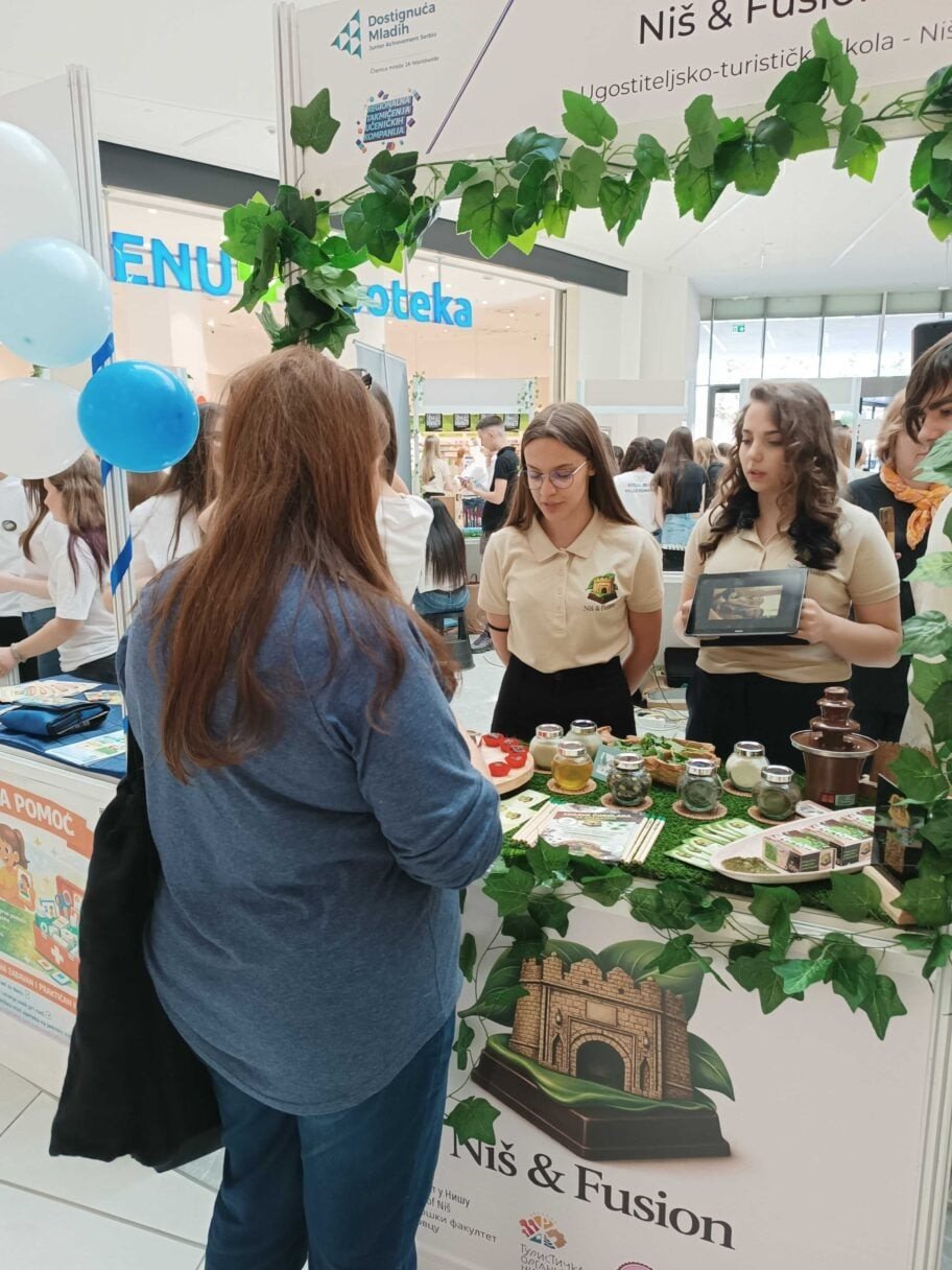 Ученицы представляют проект «Niš & Fusion» на выставочном стенде, демонстрируя продукцию и макет шоколадной крепости