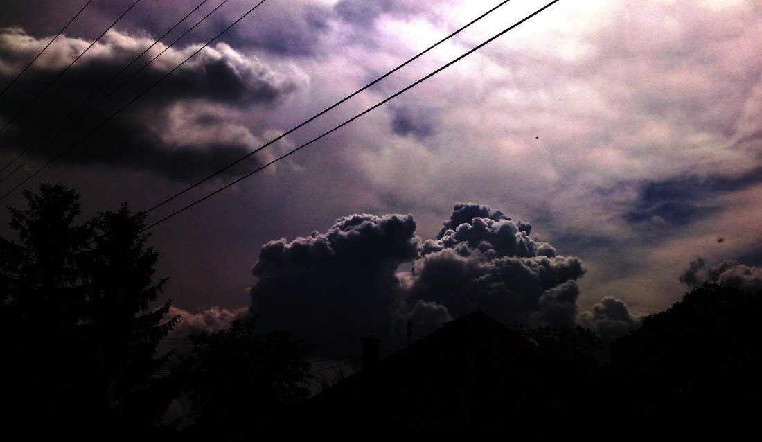 Тёмные грозовые тучи нависают над силуэтами крыш и деревьев на фоне линий электропередач