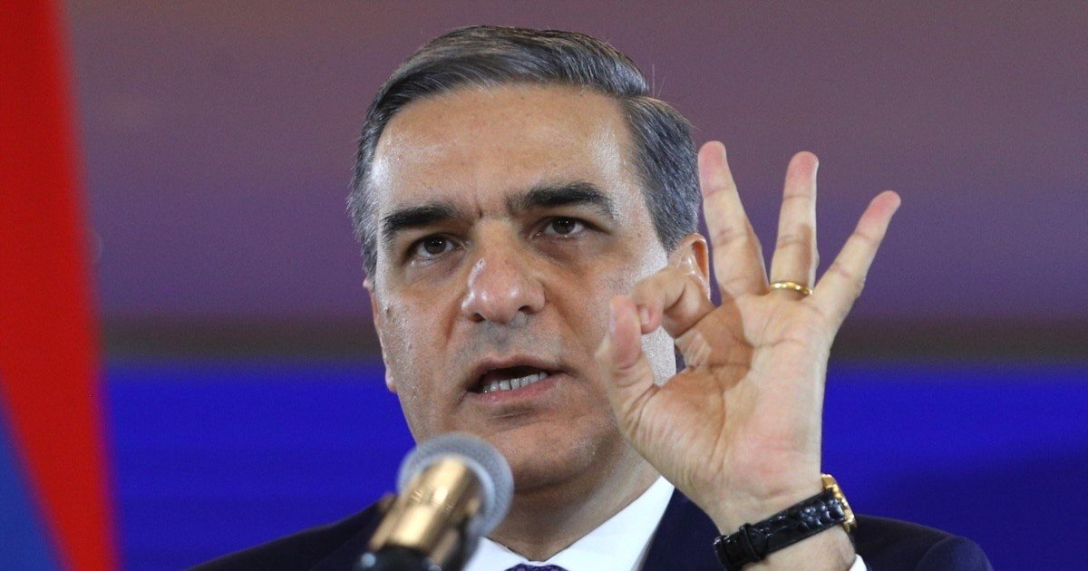 Арман Татоян выступает на пресс-конференции, жестикулируя у микрофона на фоне армянского флага