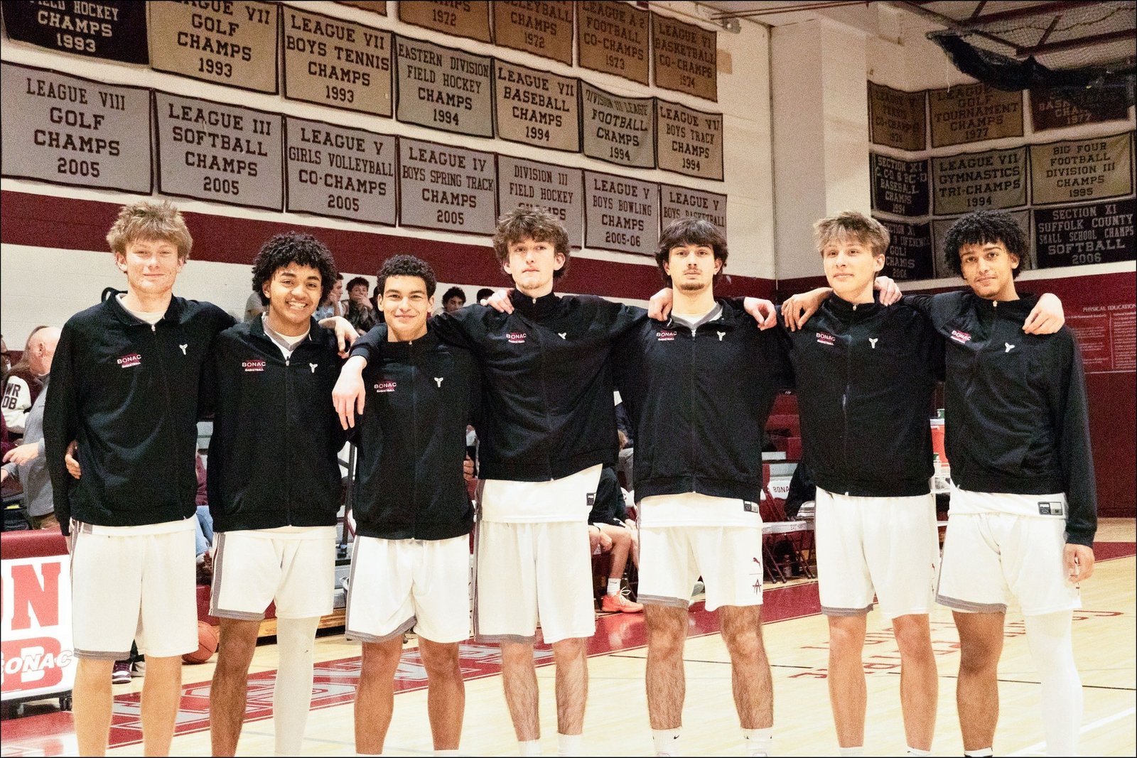 Восемь выпускников баскетбольной команды Ист-Хэмптон позируют вместе на домашней площадке во время прощального вечера