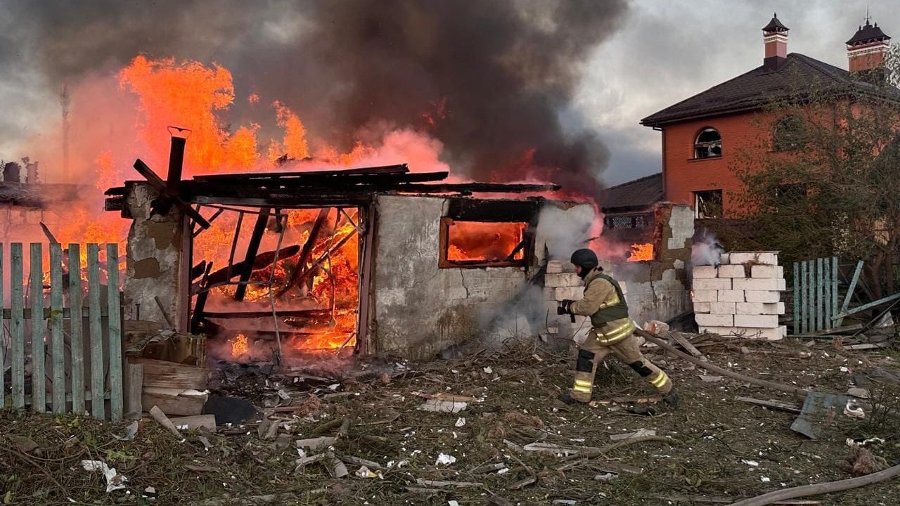Пожарный тушит горящее здание, разрушенное в результате военного удара