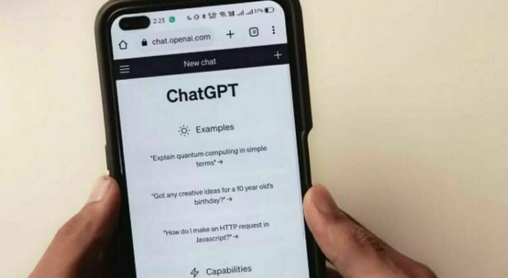 Пользователь держит в руках смартфон с открытым в браузере интерфейсом ChatGPT: заглавный экран с заголовком «New chat» и примерами запросов