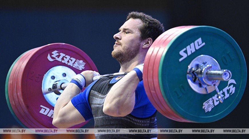 Тяжелоатлет фиксирует штангу с красно-зелёными дисками на груди во фронтальной фазе толчка на помосте континентального чемпионата