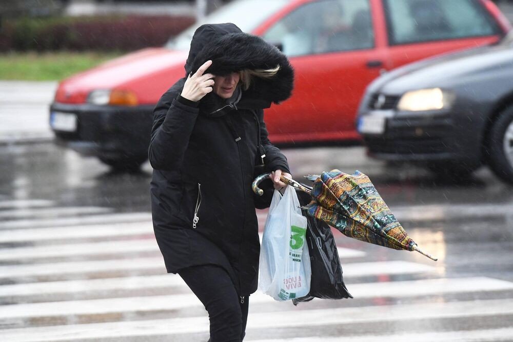 Женщина борется с порывами ветра и дождём на пешеходном переходе, держа сломанный зонт