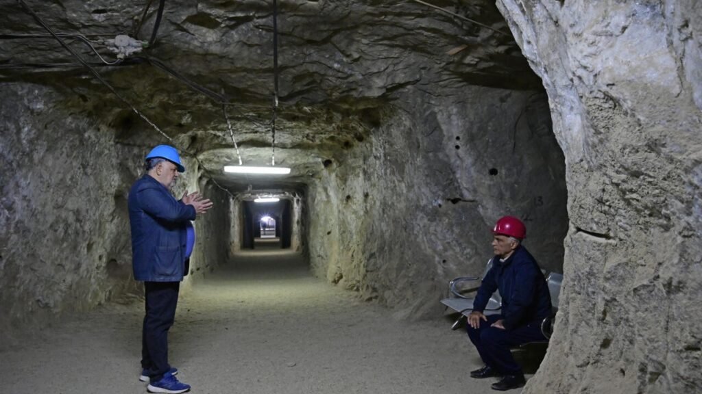 Двое мужчин в защитных касках разговаривают в подземном тоннеле Аванской соляной шахты под Ереваном, где расположена клиника спелеотерапии