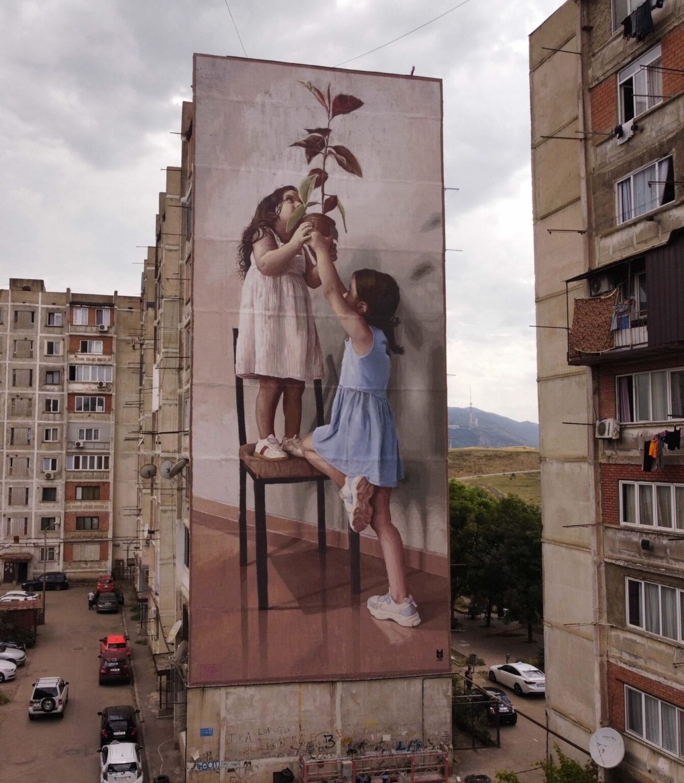 Мурал «Растение против бетона» итальянского художника Эдоардо Этторре на стене жилого дома в Тбилиси: две девочки тянутся к зелёному ростку