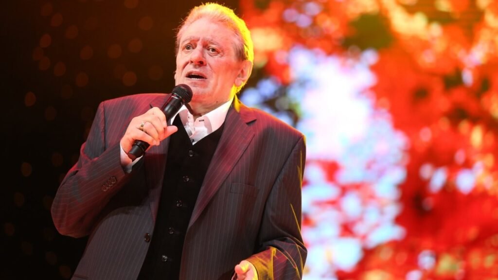 Михаил Белчев выступает на сцене с микрофоном на фоне яркой красной подсветки