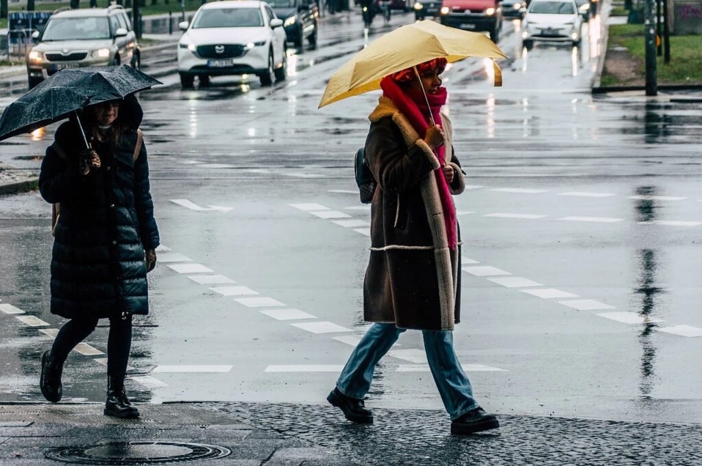 Пешеходы с зонтами переходят дорогу под проливным дождём в румынском городе