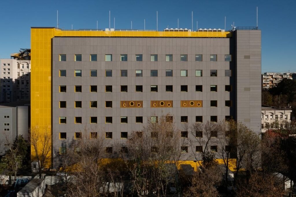 Новый корпус детской онкогематологической больницы «Dăruiește Viață» в Бухаресте с жёлто-серым фасадом и круглыми окнами-иллюминаторами