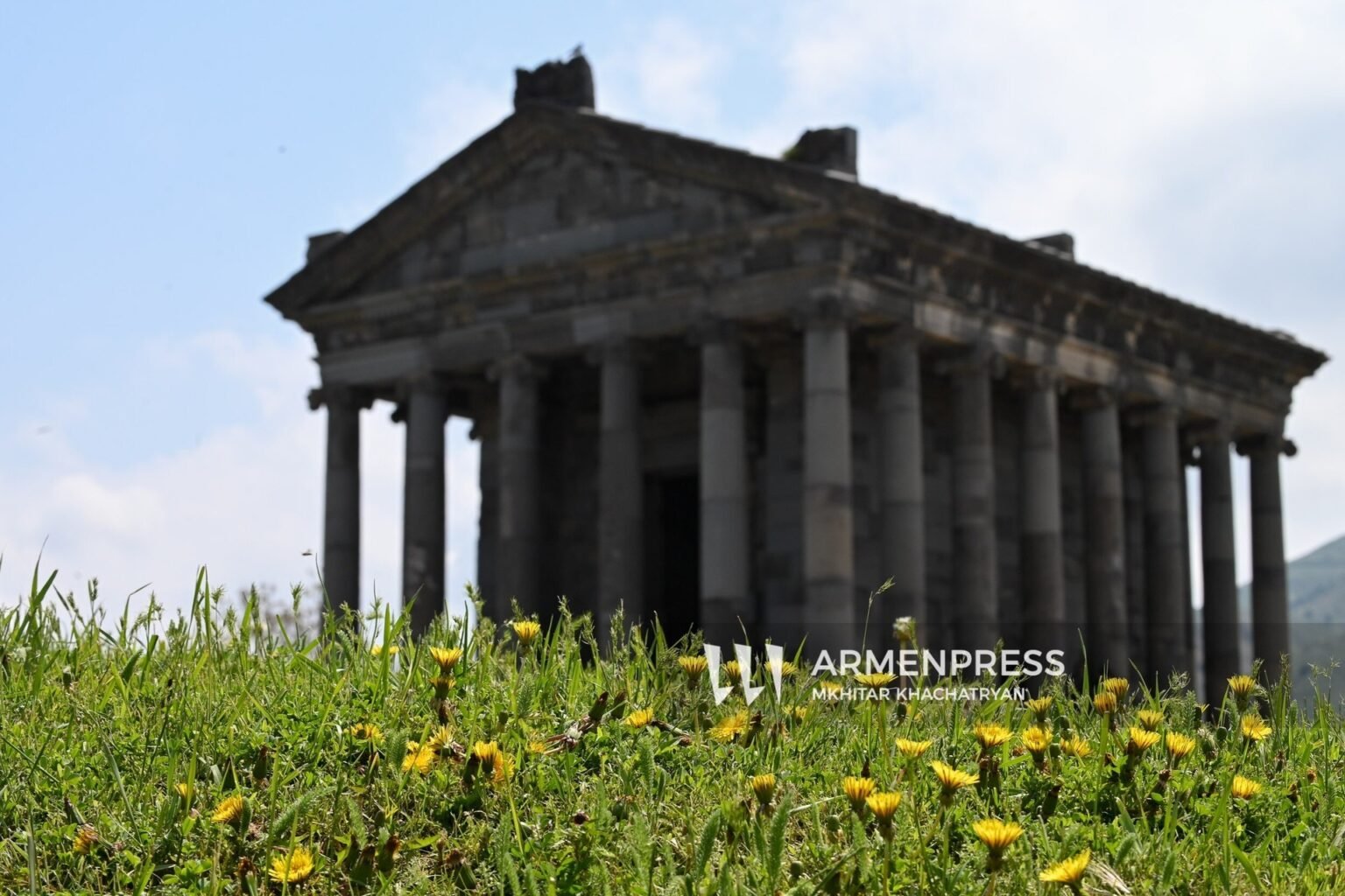 Античный храм Гарни в Армении с колоннами и фронтоном на фоне весенней зелени и одуванчиков