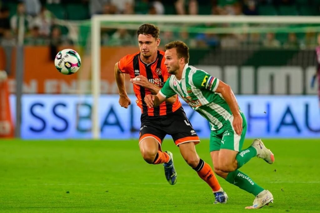 Юрий Иову в оранжевой форме Dundee United борется за мяч с игроком Rapid Wien