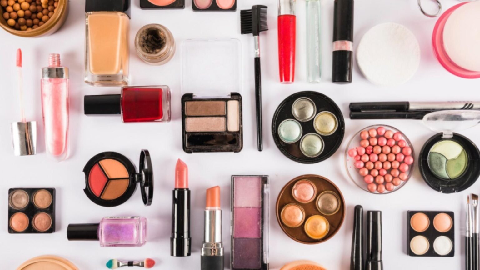 Плоская раскладка декоративной косметики — помады, тени, пудры и лаки для ногтей на белом фоне, иллюстрирующая ассортимент, попадающий под новые европейские ограничения