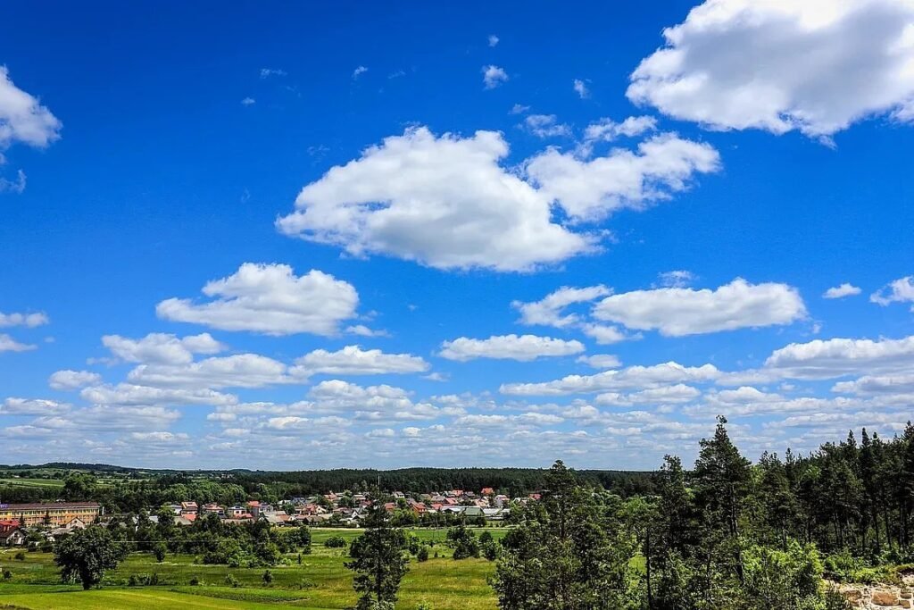 Переменная облачность над болгарским селом: белые кучевые облака на ярко-синем небе над зелёными полями и хвойным лесом — типичная картина тёплого утра 19 апреля в центральной Болгарии