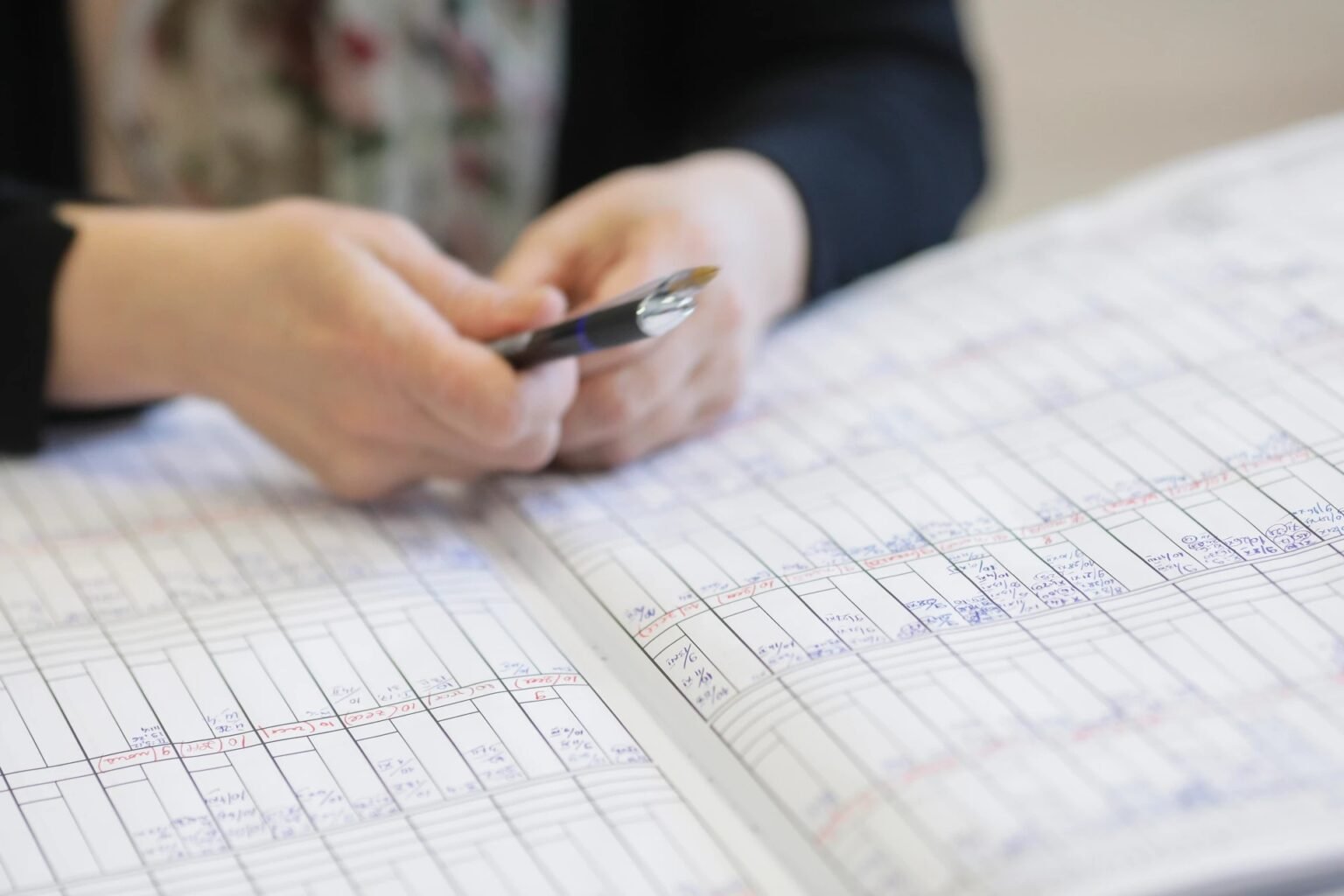 Руки учителя с ручкой над раскрытым журналом с рукописными оценками