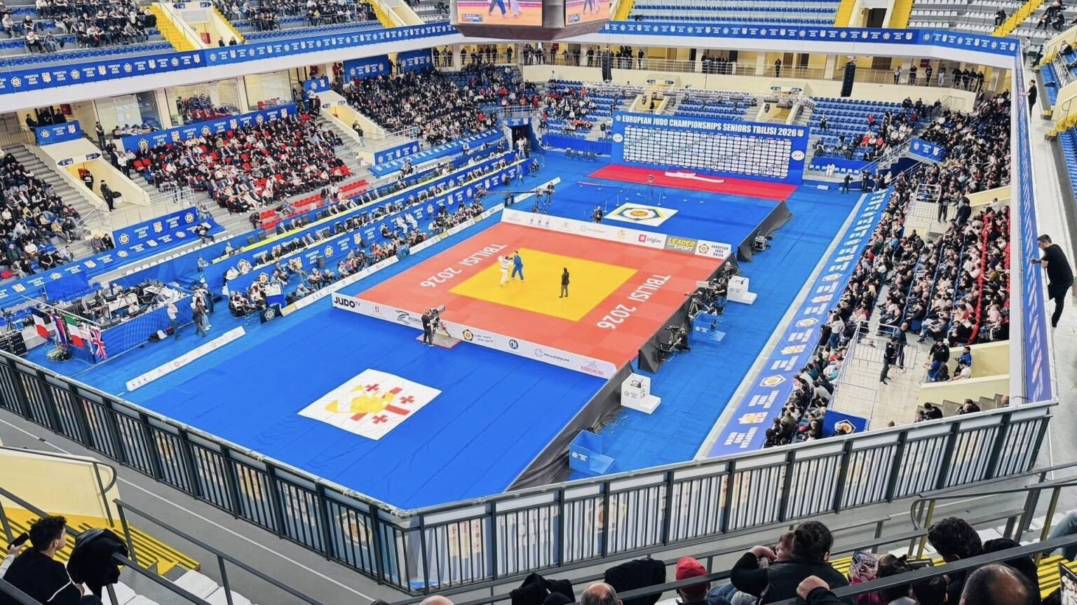 Общий план арены в Тбилиси во время чемпионата Европы по дзюдо среди взрослых 2026 года: татами в центре зала, трибуны с тысячами зрителей и баннеры турнира