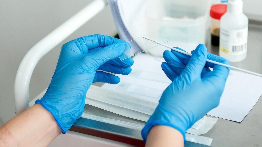 Медицинский работник в синих перчатках готовит предметное стекло с биологическим образцом — иллюстрация лабораторной работы на фоне кампании вакцинации ROR против кори, свинки и краснухи