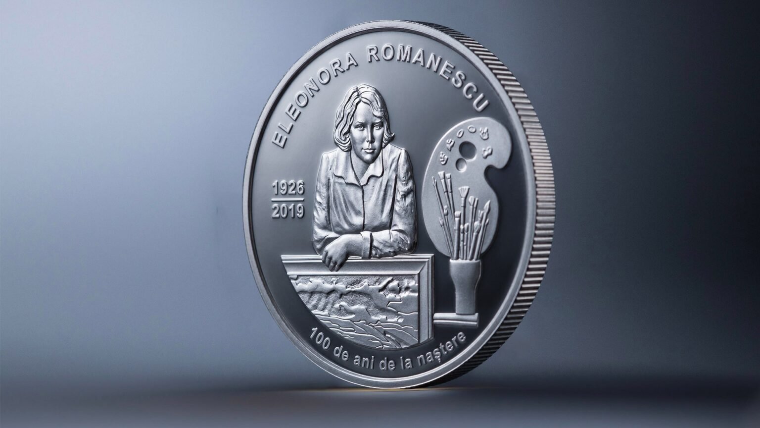 Серебряная памятная монета номиналом 50 леев, выпущенная к 100-летию Элеоноры Романеску: на реверсе — рельефный портрет художницы (1926–2019) с палитрой, кистями и пейзажем в раме, по окружности надпись «ELEONORA ROMANESCU · 100 de ani de la naștere»