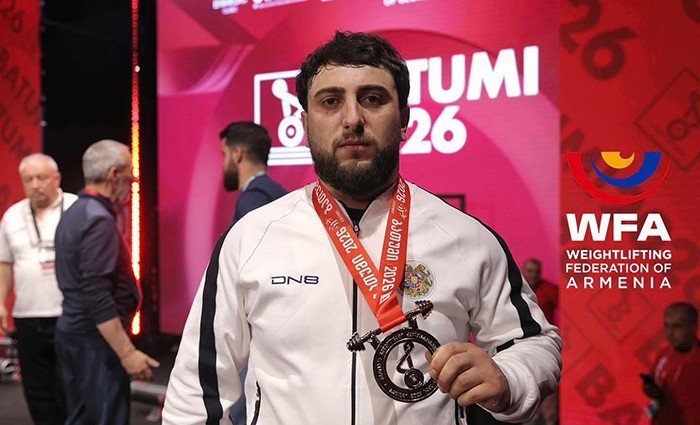 Армянский тяжелоатлет в белой олимпийке сборной Армении с медалью на сцене чемпионата Европы 2026 в Батуми