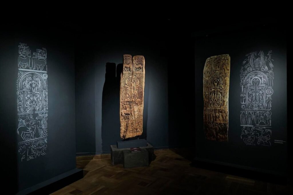 В Ереване впервые показали средневековую дверную панель XII века Панорамный вид выставочного зала Музея истории Армении: средневековая деревянная дверная панель установлена в центре на каменном постаменте, по бокам — крупные настенные проекции с контурными схемами обеих сторон артефакта