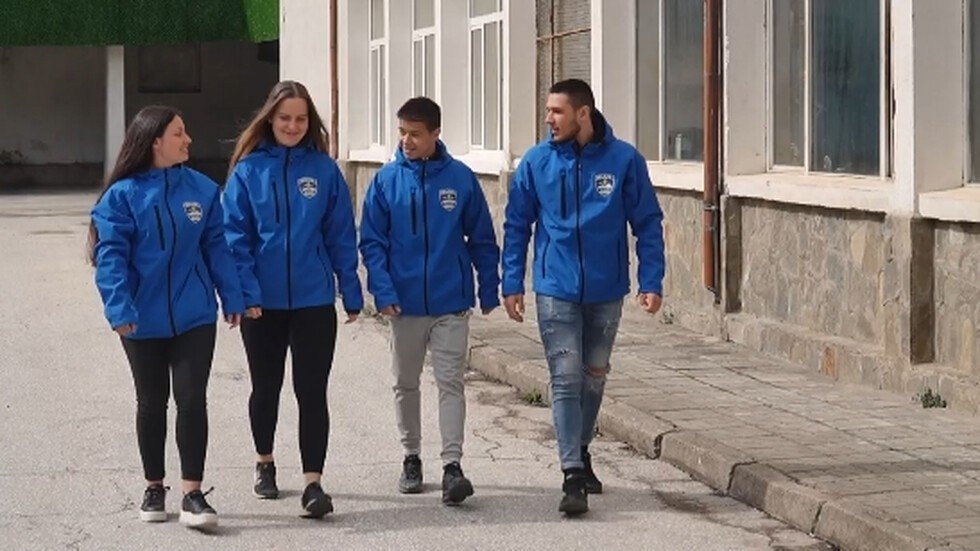 Четверо участников команды в синих куртках идут по территории школы в Чепеларе