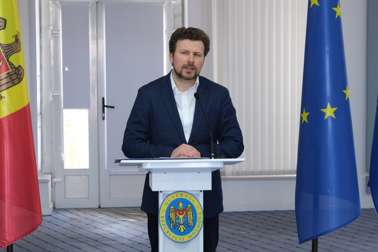 Представитель Министерства образования и науки Молдовы выступает на брифинге на фоне флагов Молдовы и Евросоюза
