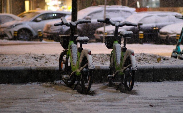 Припаркованные городские велосипеды, засыпанные снегом, на зимней улице вечером