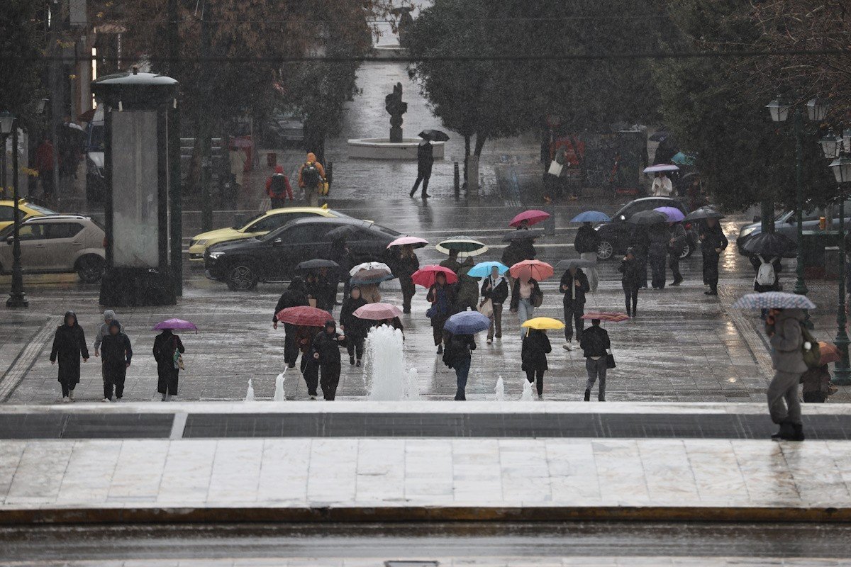 Прохожие с разноцветными зонтами идут под проливным дождём по центральной площади Афин