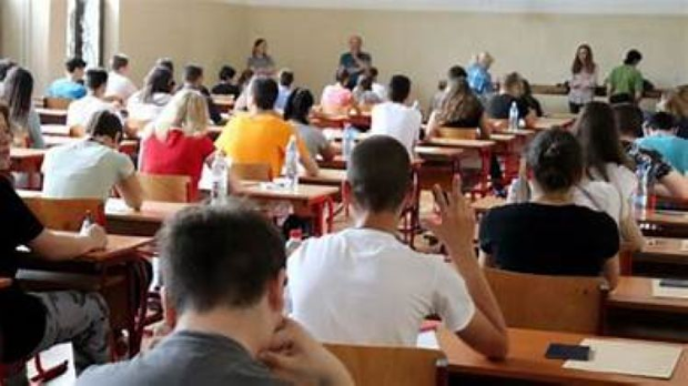 Ученики сидят за партами в классе во время пробного экзамена — один из них поднимает руку