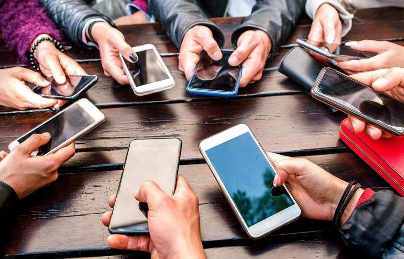 Группа подростков со смартфонами за столом — символ зависимости молодёжи от гаджетов
