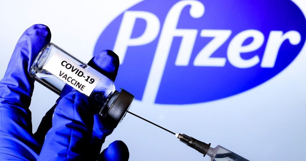 Флакон с вакциной Pfizer от COVID-19 и шприц на фоне логотипа компании
