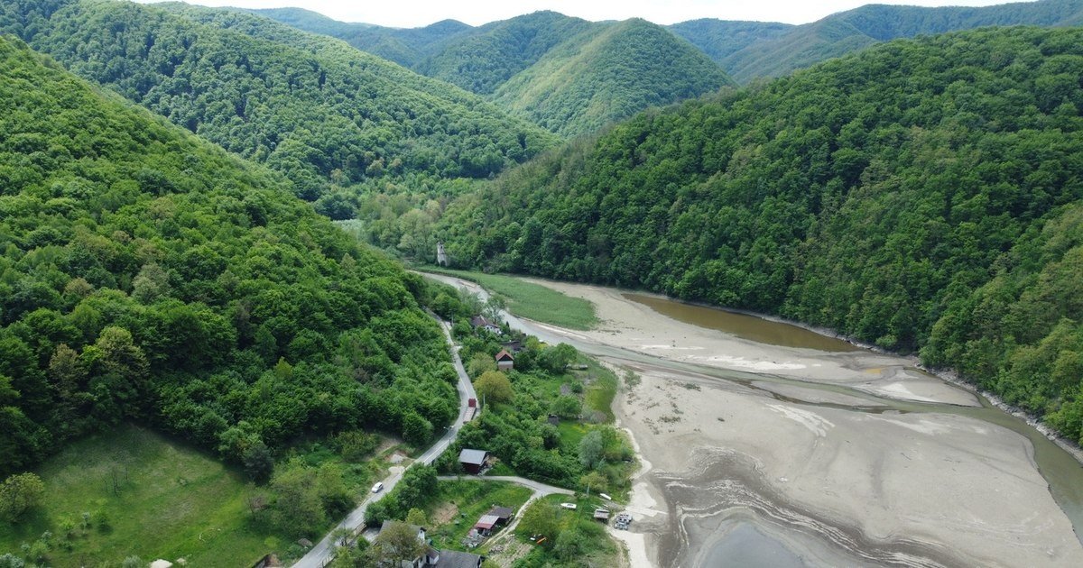 Обмелевшее водохранилище в горах Румынии — аэросъёмка долины с практически высохшим руслом среди зелёных склонов