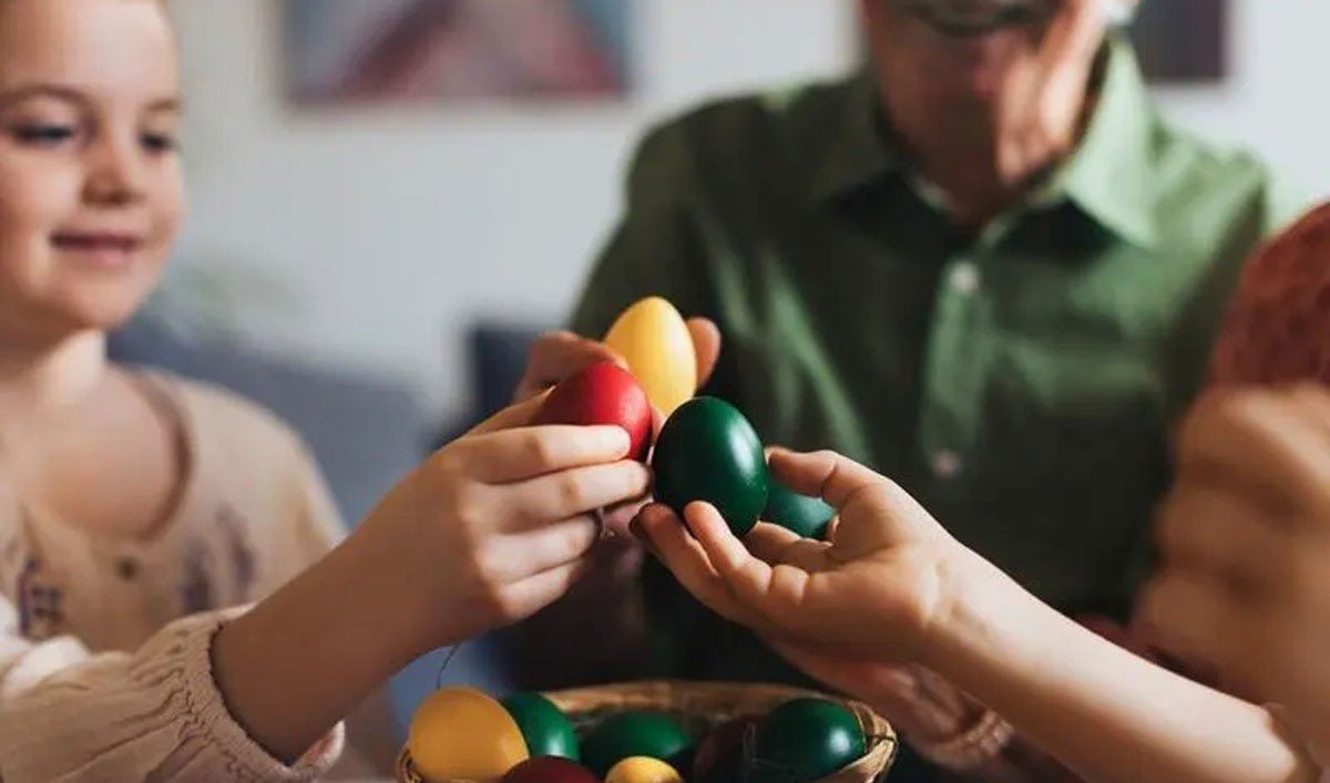 Девочка и пожилой мужчина держат крашеные пасхальные яйца за праздничным столом — кадр, которым Logos Press иллюстрирует материал о демографическом спаде в Молдове и о поредевших семейных застольях из-за эмиграции