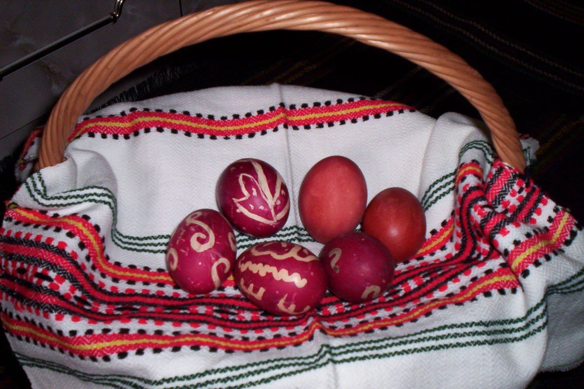 Крашеные красные яйца с восковыми узорами в плетёной корзине на молдавском рушнике