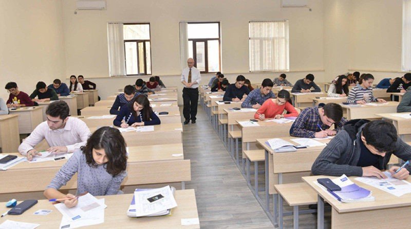 Десятки участников централизованного экзамена пишут работы за партами в просторной аудитории, пока наблюдатель обходит ряды