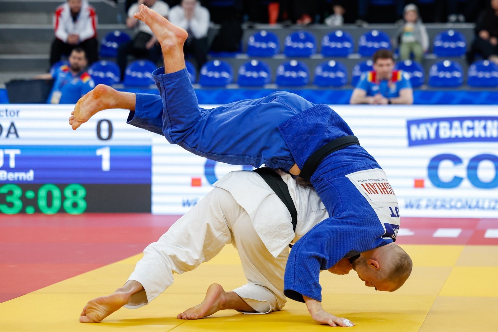 Финальный бросок на татами чемпионата Европы по дзюдо в Тбилиси 2026: спортсмен в синем кимоно выполняет бросок соперника в белом на фоне пустых зрительских рядов арены