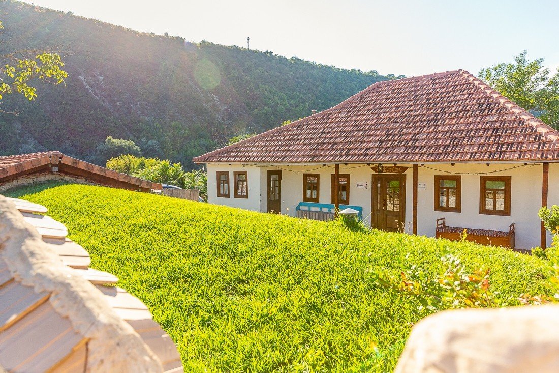 Традиционный молдавский сельский гостевой дом с черепичной крышей, побелённым фасадом и зелёной лужайкой на фоне холмов заповедника «Старый Орхей»