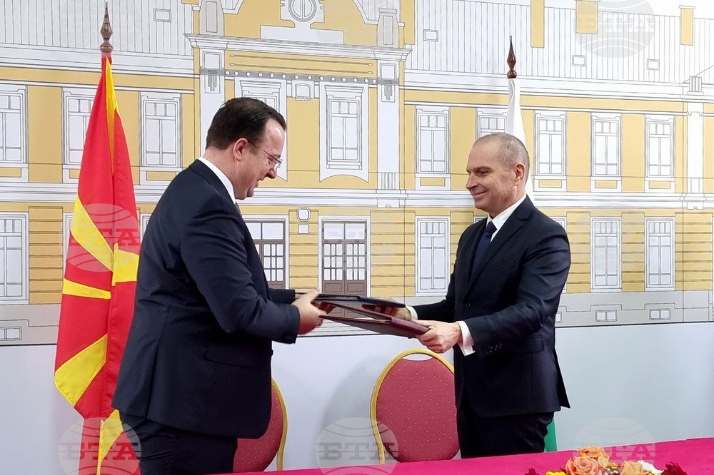 Министры обмениваются подписанными документами по железнодорожному участку Крива-Паланка–граница с Болгарией на фоне флагов Северной Македонии и Болгарии
