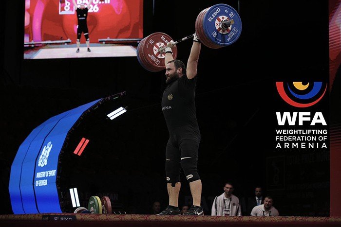 Армянский тяжелоатлет в чёрном комбинезоне фиксирует штангу над головой в рывке на помосте чемпионата Европы 2026 в Батуми