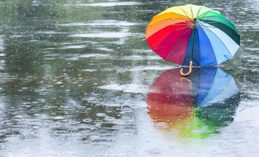 Радужный зонт лежит на мокром асфальте во время сильного дождя, отражаясь в лужах