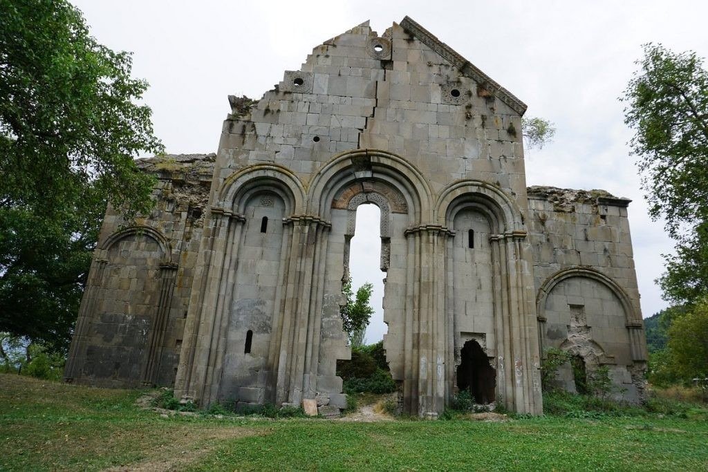 Руины грузинской церкви с монументальными арочными проёмами на зелёном склоне холма в Артвине