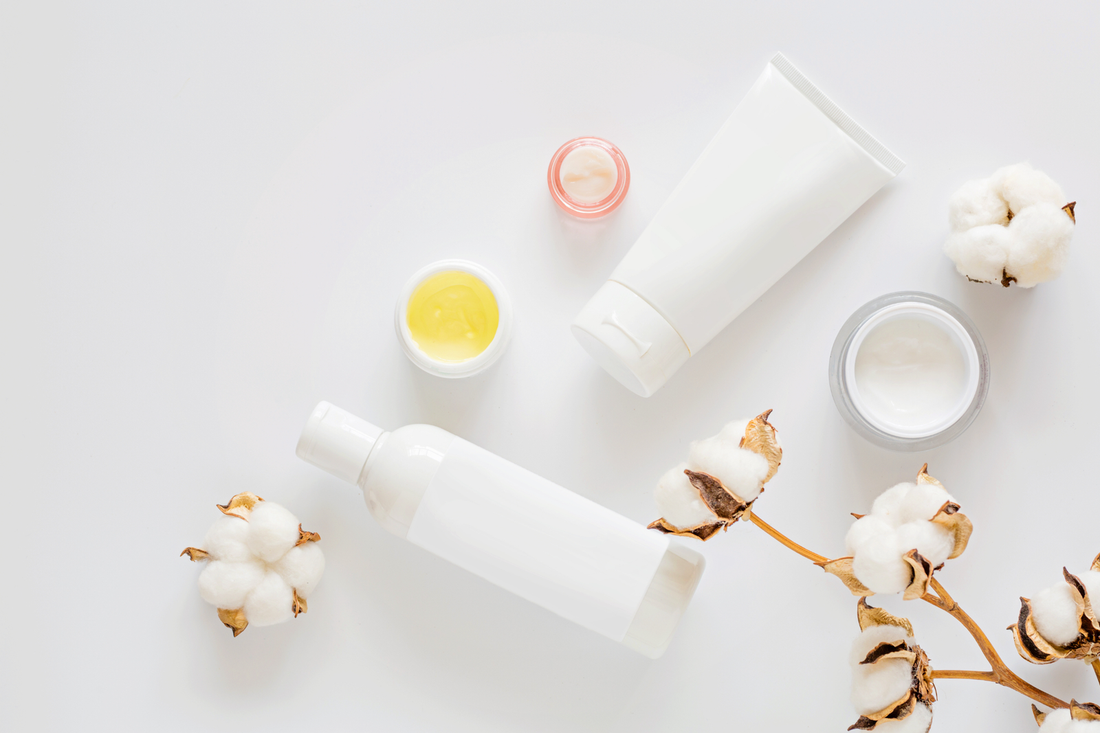 Тюбики и баночки средств по уходу с цветками хлопка на светлом фоне — типовой ассортимент, на который распространяются новые правила состава