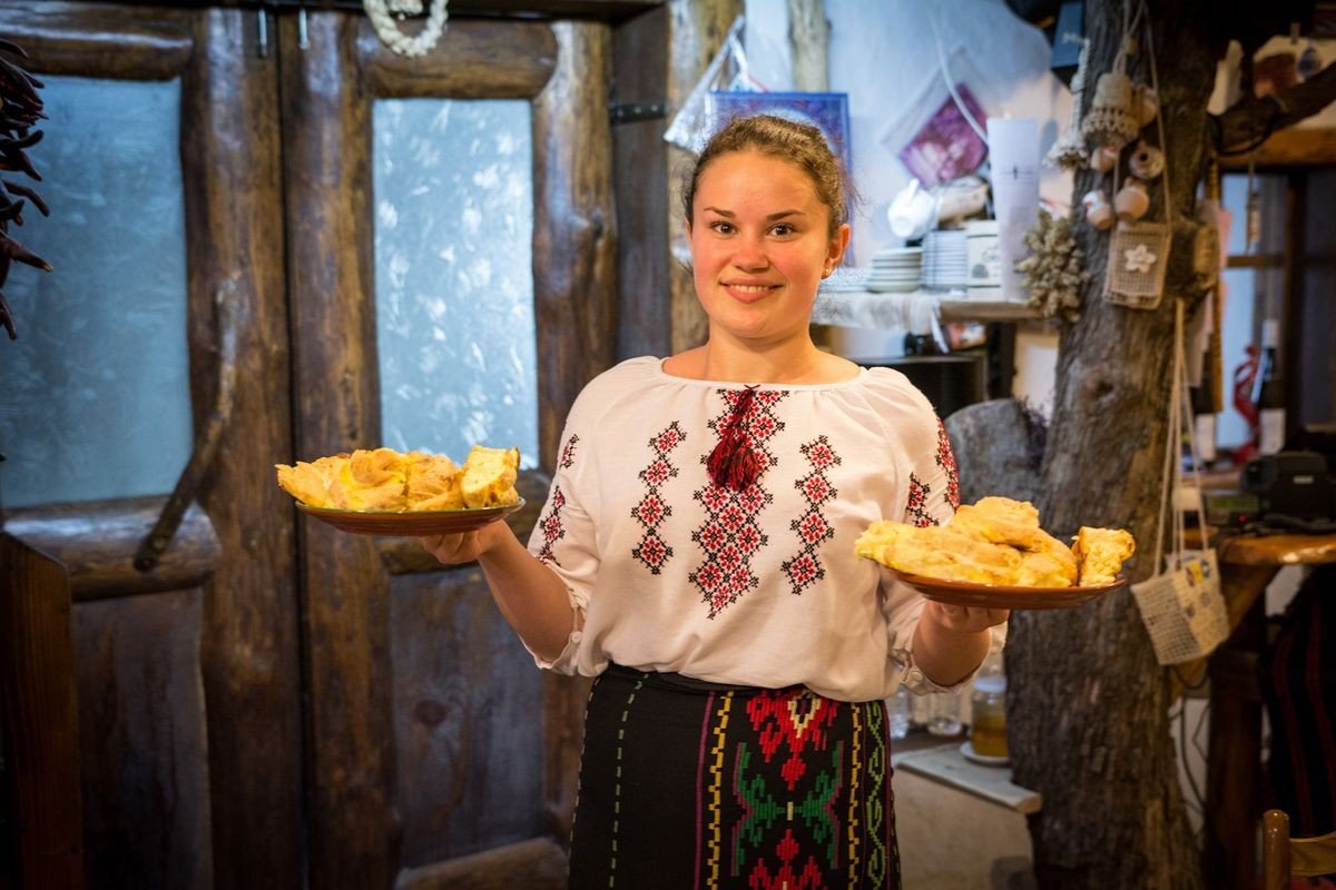 Хозяйка сельской усадьбы в традиционной молдавской вышиванке держит два подноса со свежеиспечёнными плэчинтами — угощает гостей в гостевом доме под Старым Орхеем