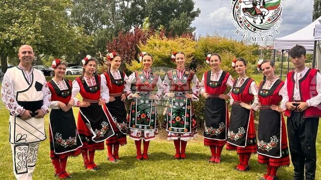 Болгарский танцевальный коллектив в традиционных костюмах с красно-белой вышивкой — иллюстрация культурного обмена и туристического потенциала, который усилит новая железнодорожная линия