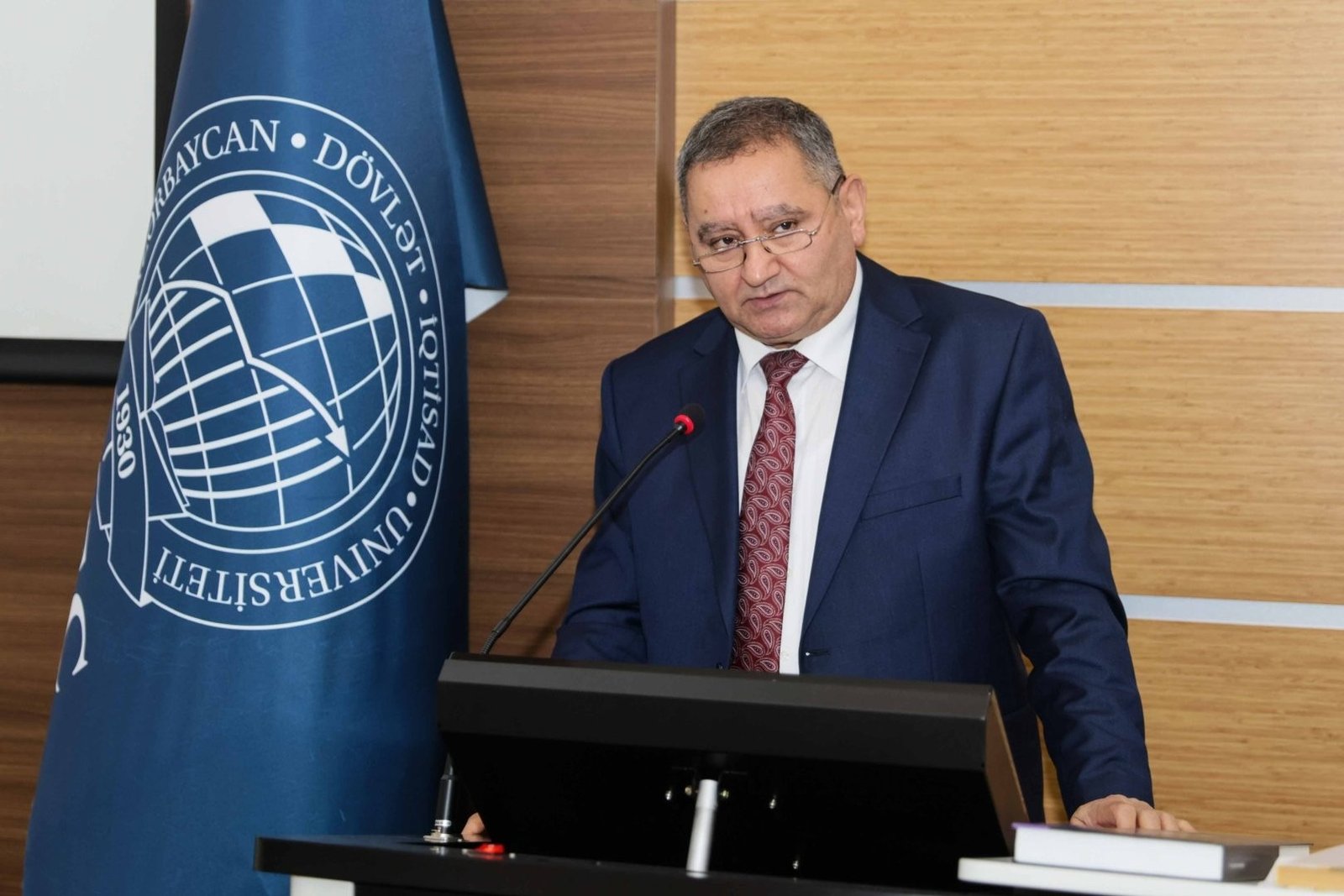 Спикер выступает за трибуной с символикой Азербайджанского государственного экономического университета (UNEC)